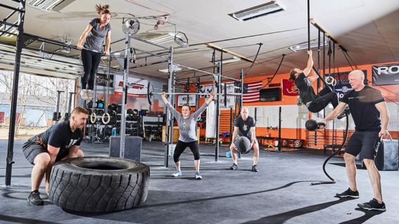 Imagem de box de CrossFit com homens e mulheres treinando.